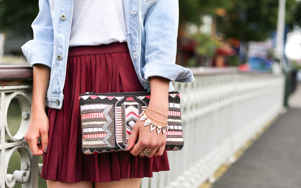 A woman in a red skirt, jean shirt, and jewelry holds a patterned clutch in Rotterdam