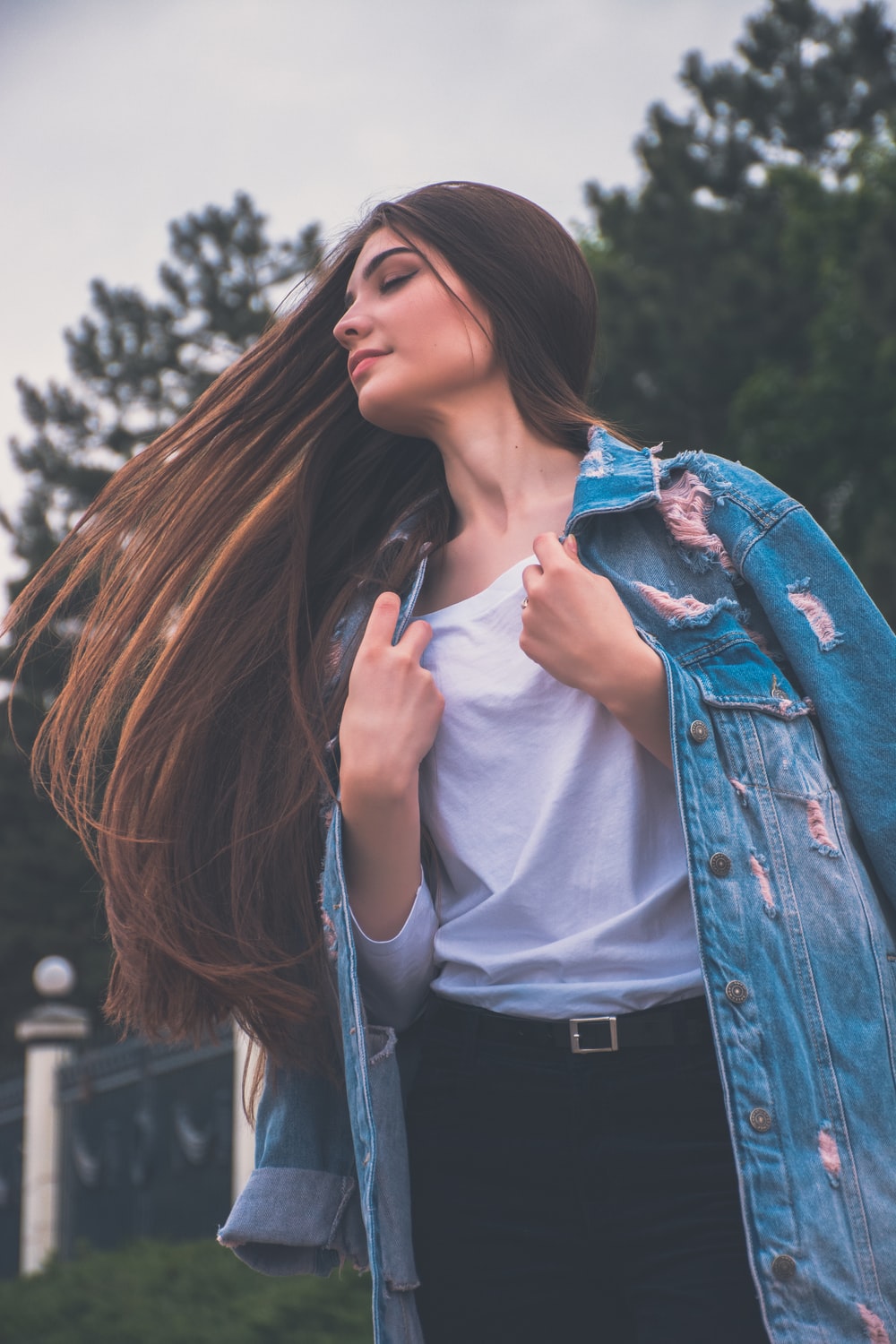 A woman in a jean coat whips her long brown hair to the side outdoors